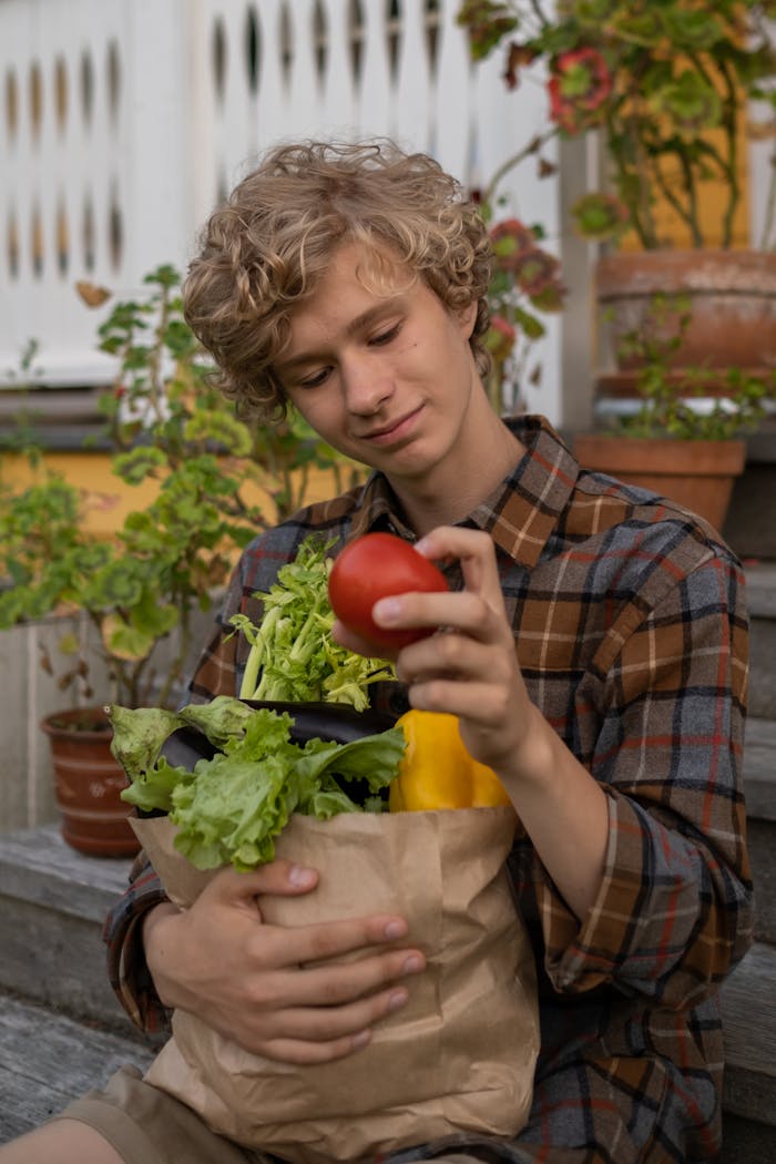 The Art of Drawing Readers In: Your attractive post title goes here Teenage boy with curly hair holding a paper bag of fresh vegetables on steps.