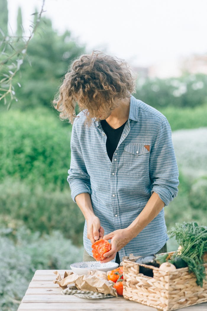 our-mission A young man cuts fresh red bell pepper at an outdoor table surrounded by greenery.