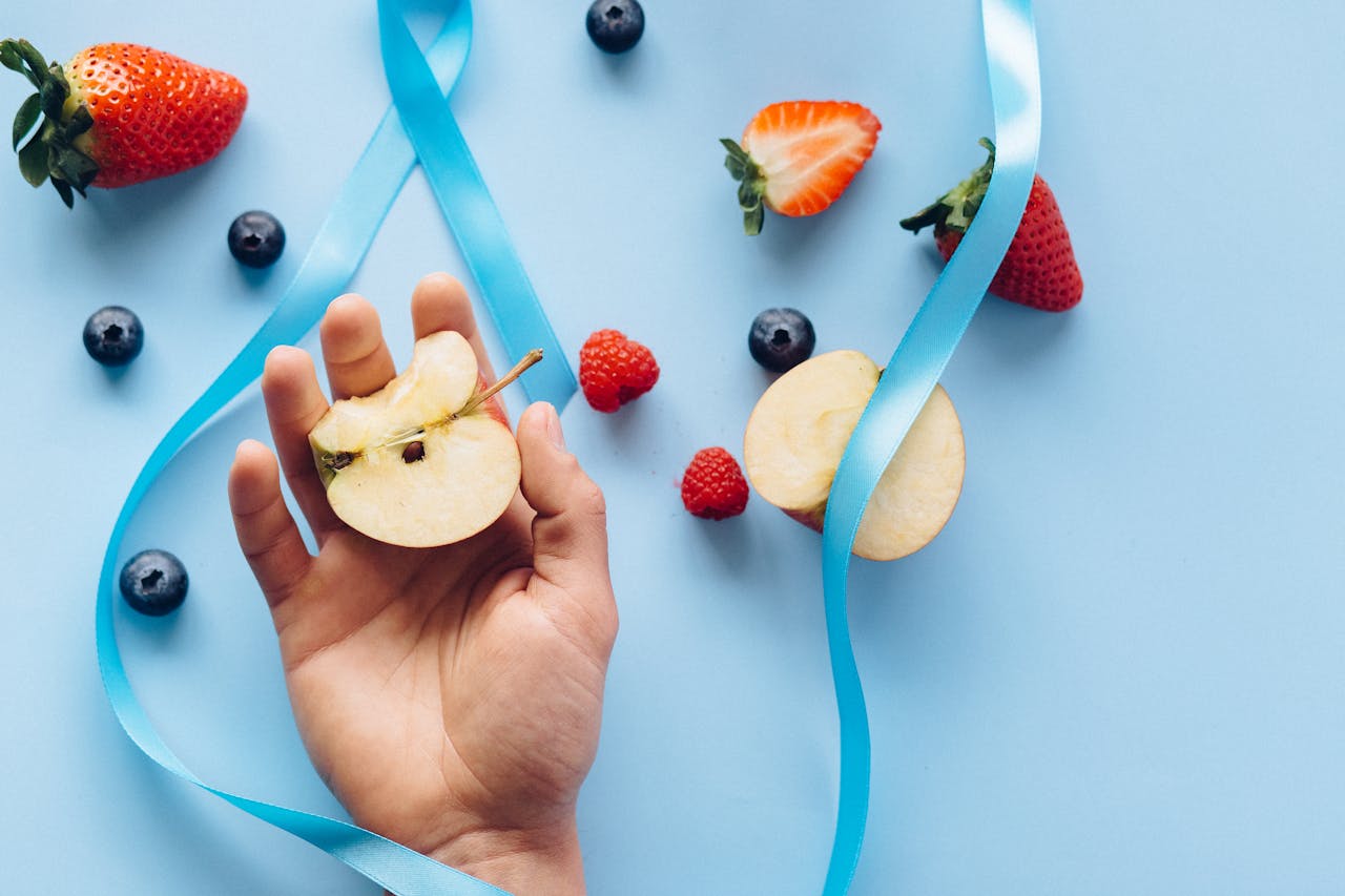 Mastering the First Impression: Your intriguing post title goes here Slice of apple in hand surrounded by strawberries, blueberries, and ribbon on blue surface.