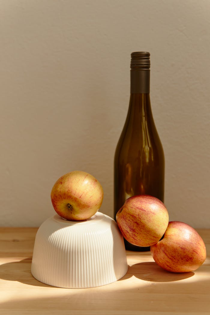 Mastering the First Impression: Your intriguing post title goes here Warm-toned still life featuring apples and a wine bottle on wooden table.